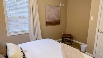 Une chambre à coucher avec un lit, une chaise, un tableau et une fenêtre avec des rideaux.