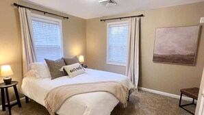 Une chambre à coucher avec un lit, deux tables de chevet, une commode, une lampe et un tableau au mur.