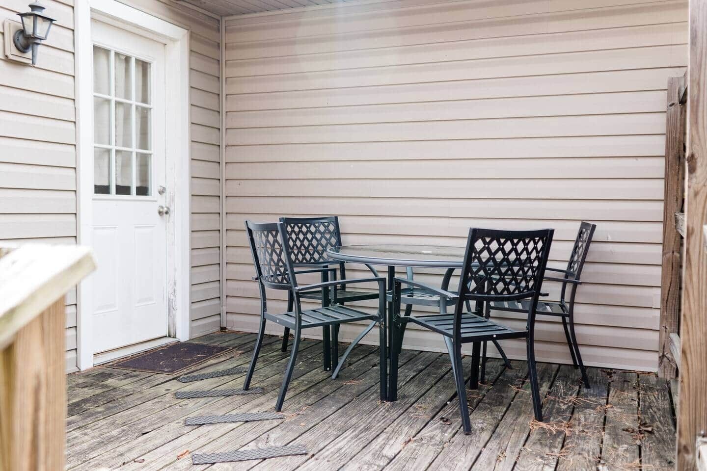 A covered patio with a table and chairs, a white door, and wooden flooring.