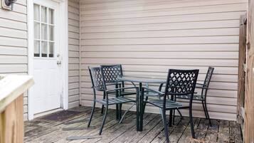 A covered patio with a table and chairs, a white door, and wooden flooring.