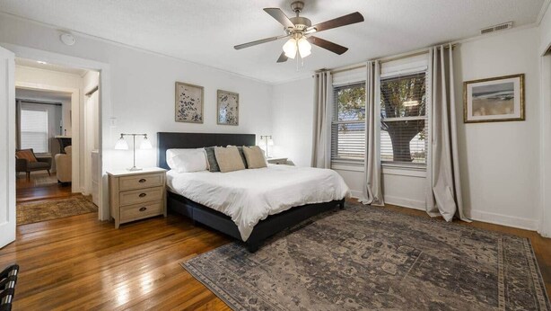 A bedroom with a bed, nightstands, a ceiling fan, and a large rug.