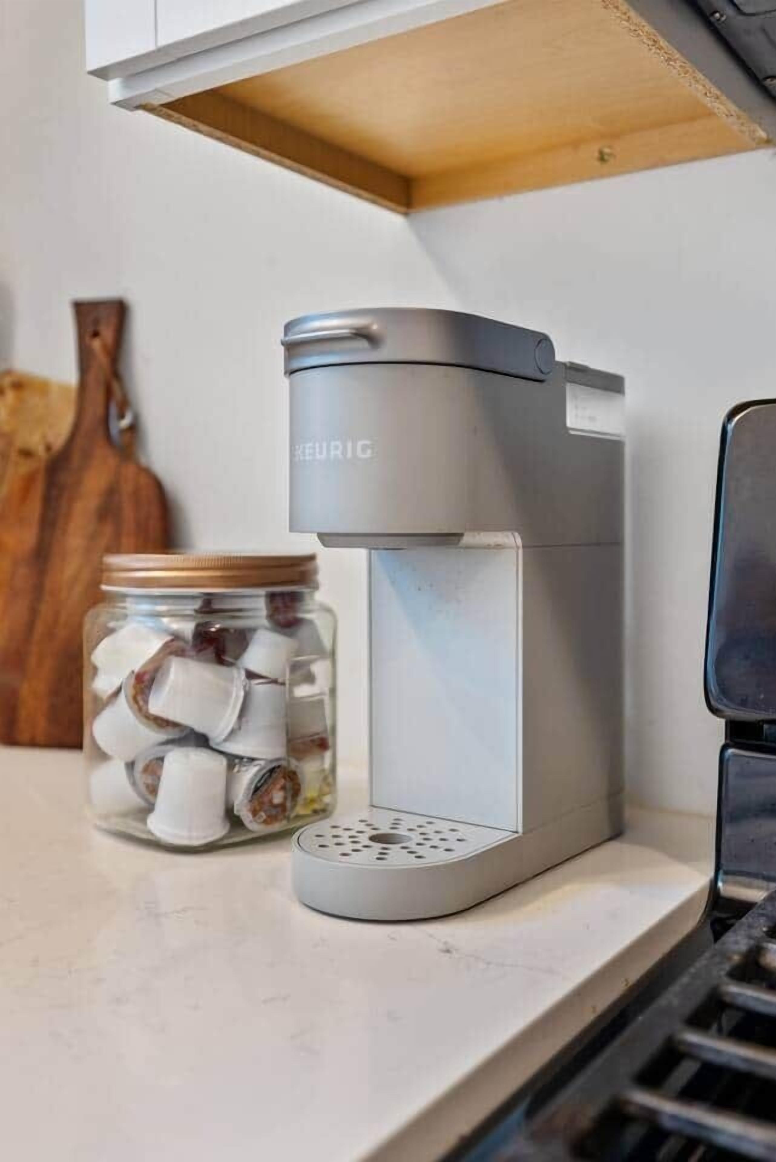 Uma cafeteira com um pote de cápsulas de café numa bancada de cozinha.