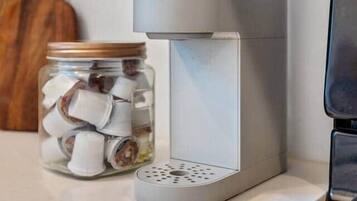 Uma cafeteira com um pote de cápsulas de café numa bancada de cozinha.