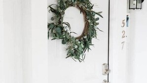 A white door with a wreath, a doorbell, and two wall-mounted lanterns.