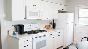 Una cocina compacta con armarios blancos, microondas, estufa y refrigerador.