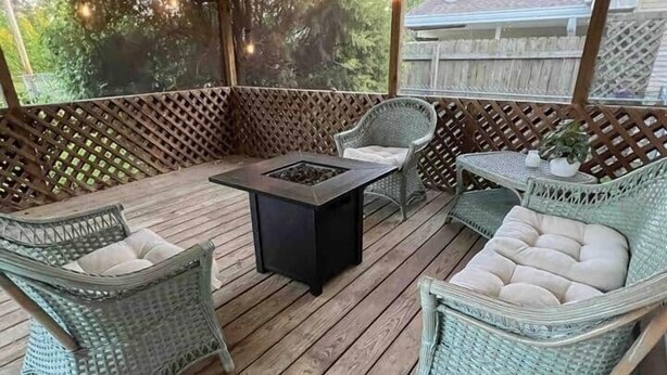 Un patio techado al aire libre con mobiliario de mimbre, una mesa central y un brasero.