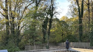 A wooden deck with wicker chairs and a grill, surrounded by trees. - 2 Bedroom Apt in Downtown ATL, Steps from Beltline (Atlanta)