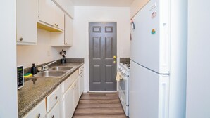 A narrow kitchen with white cabinets, a stainless steel sink, and a white refrigerator. - 2 Bedroom Apt in Downtown ATL, Steps from Beltline (Atlanta)