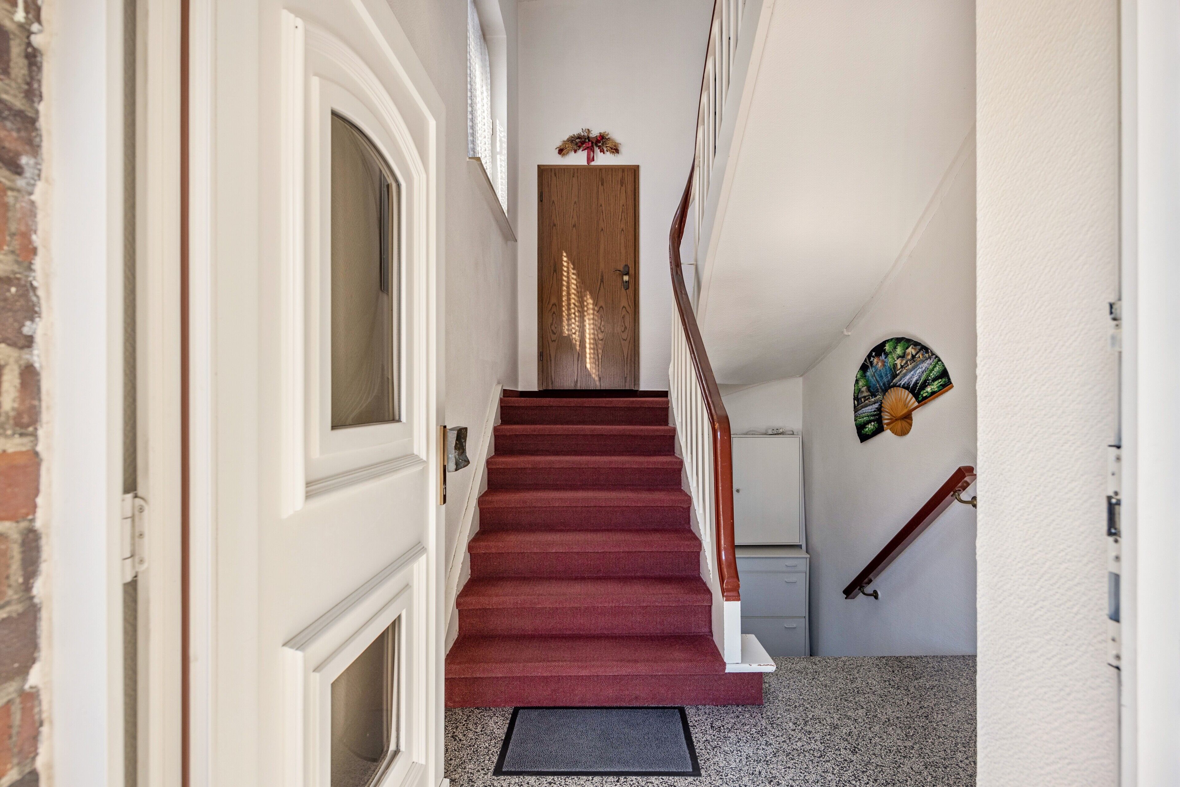 A staircase with a wooden door at the top, a white wall, and a small decorative item on the wall.