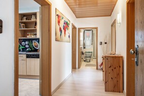 Un couloir avec une porte en bois, une cuisine équipée de placards et d’un lave-vaisselle, et une salle de bain avec des toilettes et une douche.