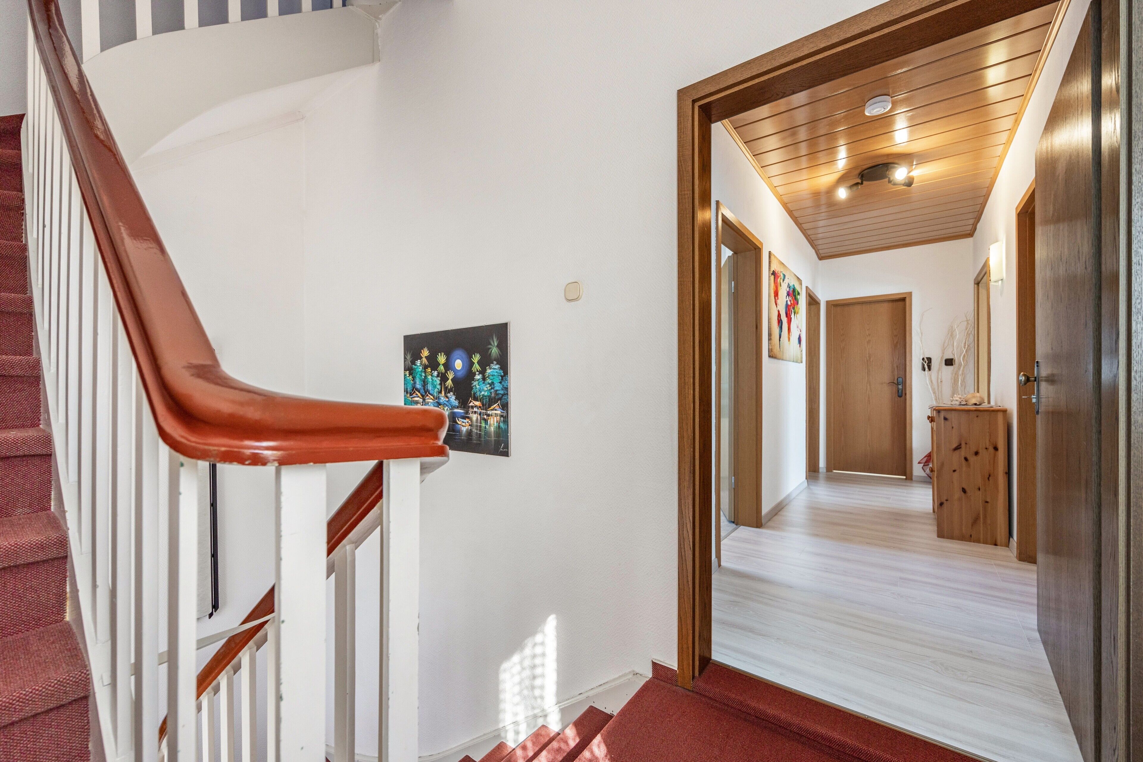 Un escalier avec une rampe en bois, une moquette rouge et une porte en bois au bout.