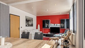 A modern living room with a wooden dining table, a red accent wall, and a large window. - Apartment 'Messe-und-Ferien-Wohnung' with Wi-Fi (Seelze)
