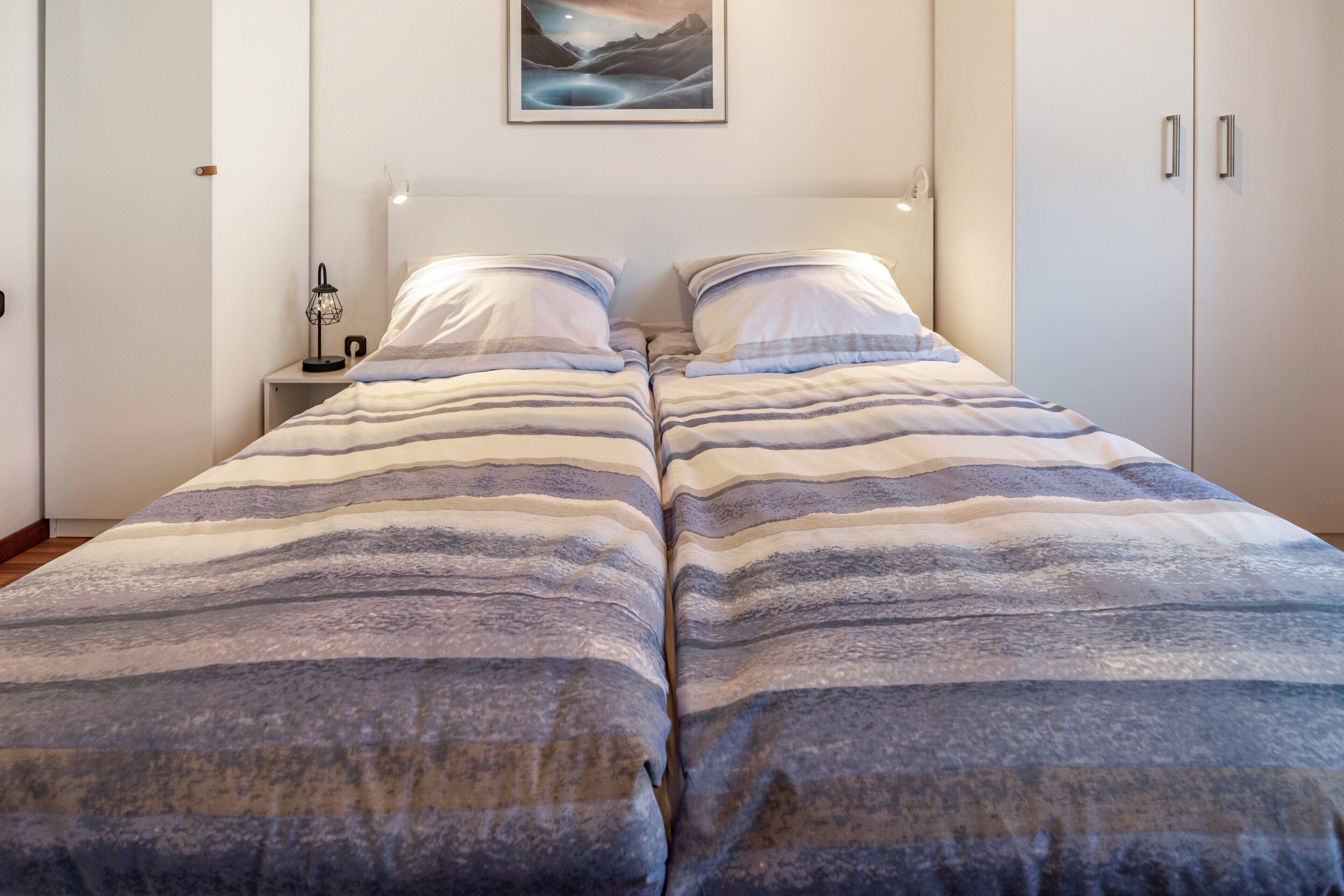 Un lit double avec une literie à rayures, une table de chevet avec une lampe et un tableau encadré au mur.