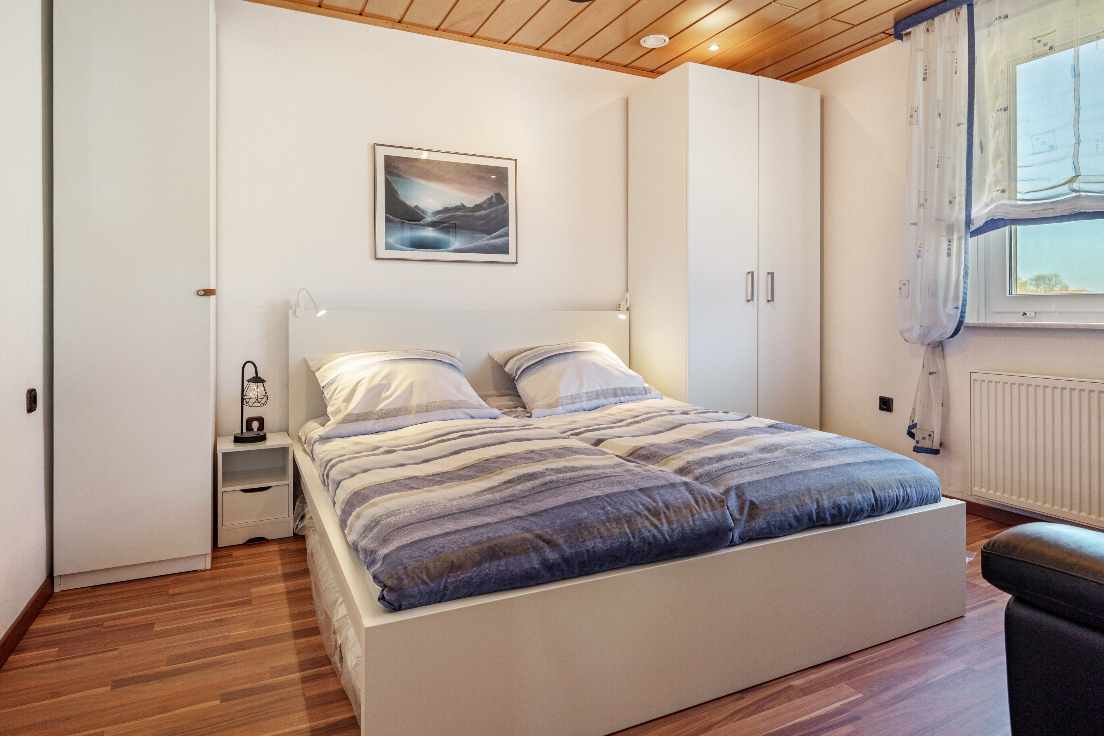Ein Schlafzimmer mit Bett, Nachttischen, einer Wandlampe, einem Fenster mit Vorhängen und einer Heizung.