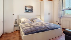 A bedroom with a bed, nightstands, a wall-mounted lamp, a window with curtains, and a radiator. - Apartment 'Messe-und-Ferien-Wohnung' with Wi-Fi (Seelze)