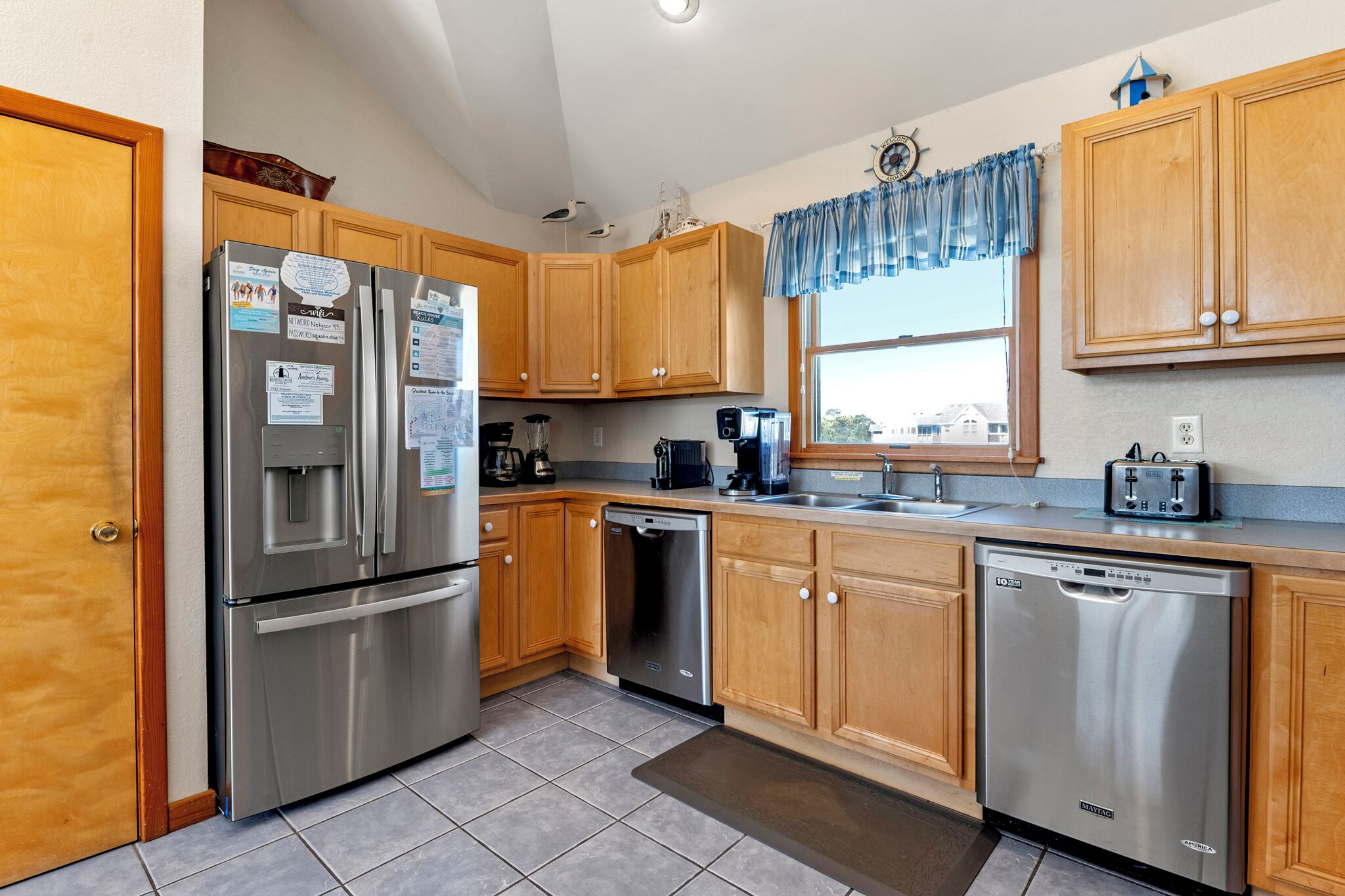 A kitchen with wooden cabinets, stainless steel appliances, and a window with a blue valance.