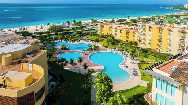 Un complexe hôtelier doté d’une grande piscine, de nombreux balcons et offrant une vue sur la plage.