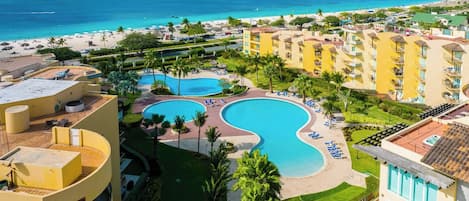 Een resort met een groot zwembad, meerdere balkons en uitzicht op het strand.