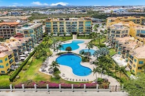 A hotel with multiple buildings, a central swimming pool, and surrounding greenery. - 3BR condo•Eagle Beach•Private balcony (Noord)
