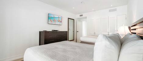 A bedroom with a large bed, a dresser, a nightstand, and a wall-mounted lamp.