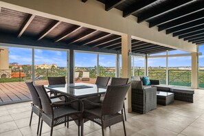 An outdoor patio with a glass-top table surrounded by wicker chairs, a sofa, and a small coffee table.