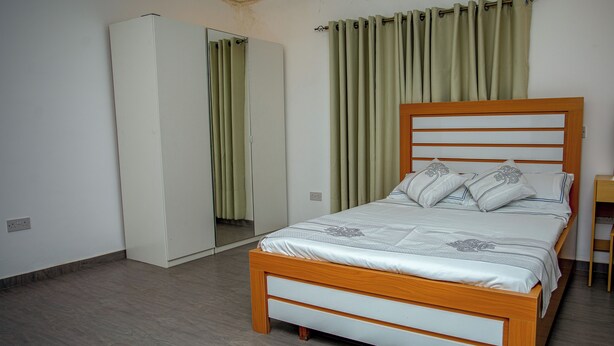 A bedroom with a wooden bed, a wardrobe, and a mirror. - Tranquil 4-bedroom apartment with AC in Dawhenya (Dawhenya)