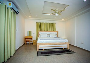 A bedroom with a bed, a bedside table, a nightstand, a ceiling fan, and a window with curtains. - Tranquil 4-bedroom apartment with AC in Dawhenya (Dawhenya)