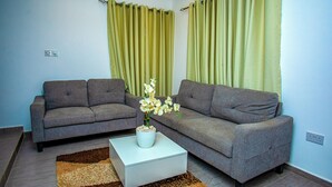 A living room with two grey sofas, a white coffee table, and a brown and beige rug. - Tranquil 4-bedroom apartment with AC in Dawhenya (Dawhenya)