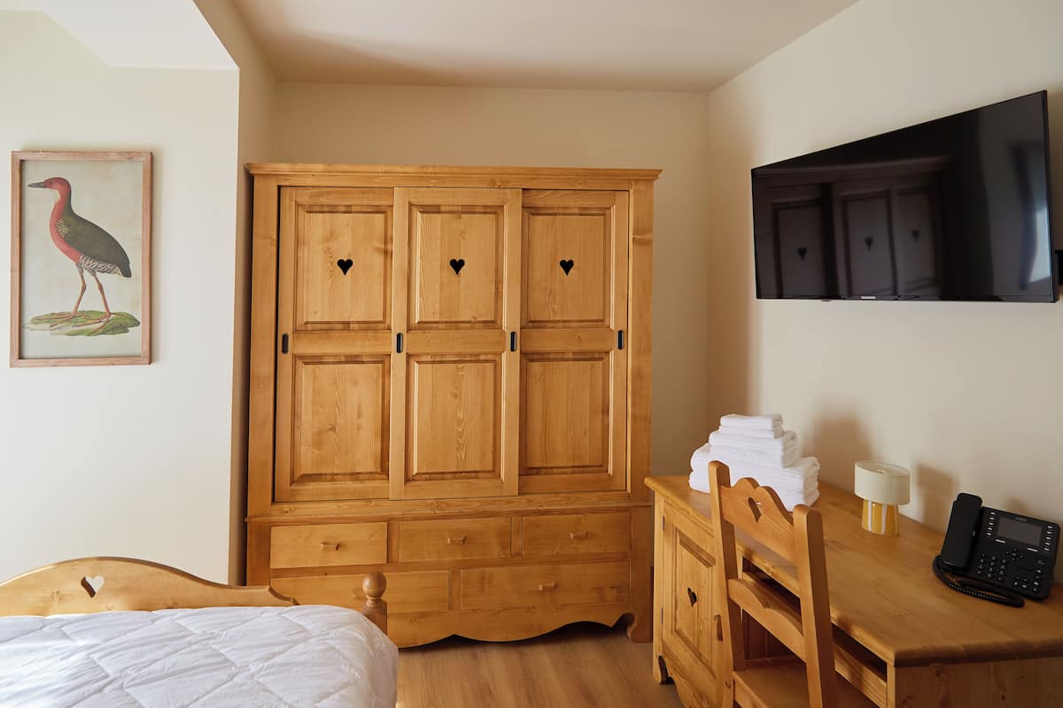 Une chambre à coucher avec une armoire en bois, un lit, un bureau avec une lampe et un téléphone.