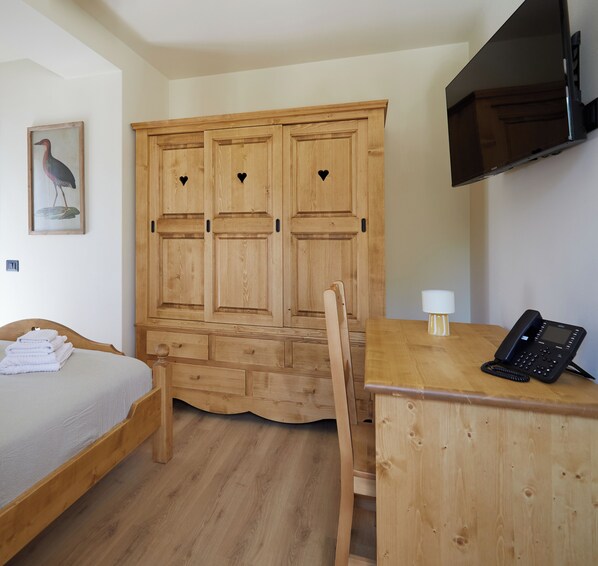 A wooden room with a bed, a desk with a phone, and a TV on the wall. - Hotel Villa Alpina (Forni di Sopra)