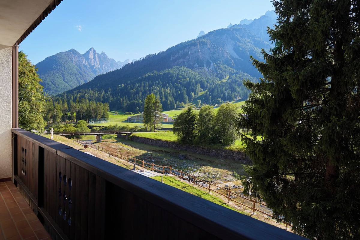 Un balcon offrant une vue sur un paysage montagneux, avec une clôture en bois et un mur de pierre.