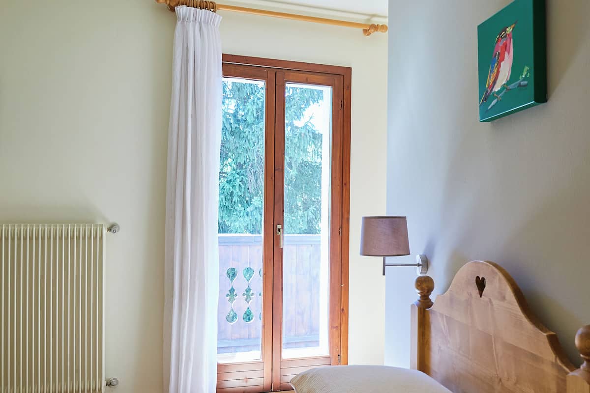 Une chambre à coucher avec un lit, une fenêtre avec des rideaux, un radiateur et une lampe fixée au mur.