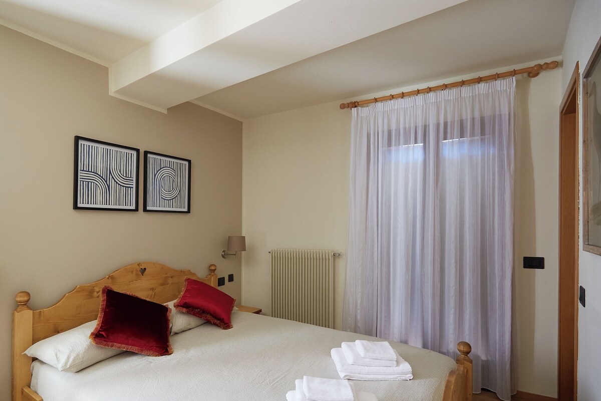 Una cama bien hecha con sábanas blancas y almohadas rojas, un cabecero de madera y un par de toallas dobladas sobre la cama.