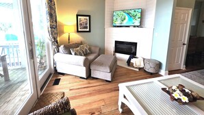 Una sala de estar con chimenea, televisor y vistas al exterior.