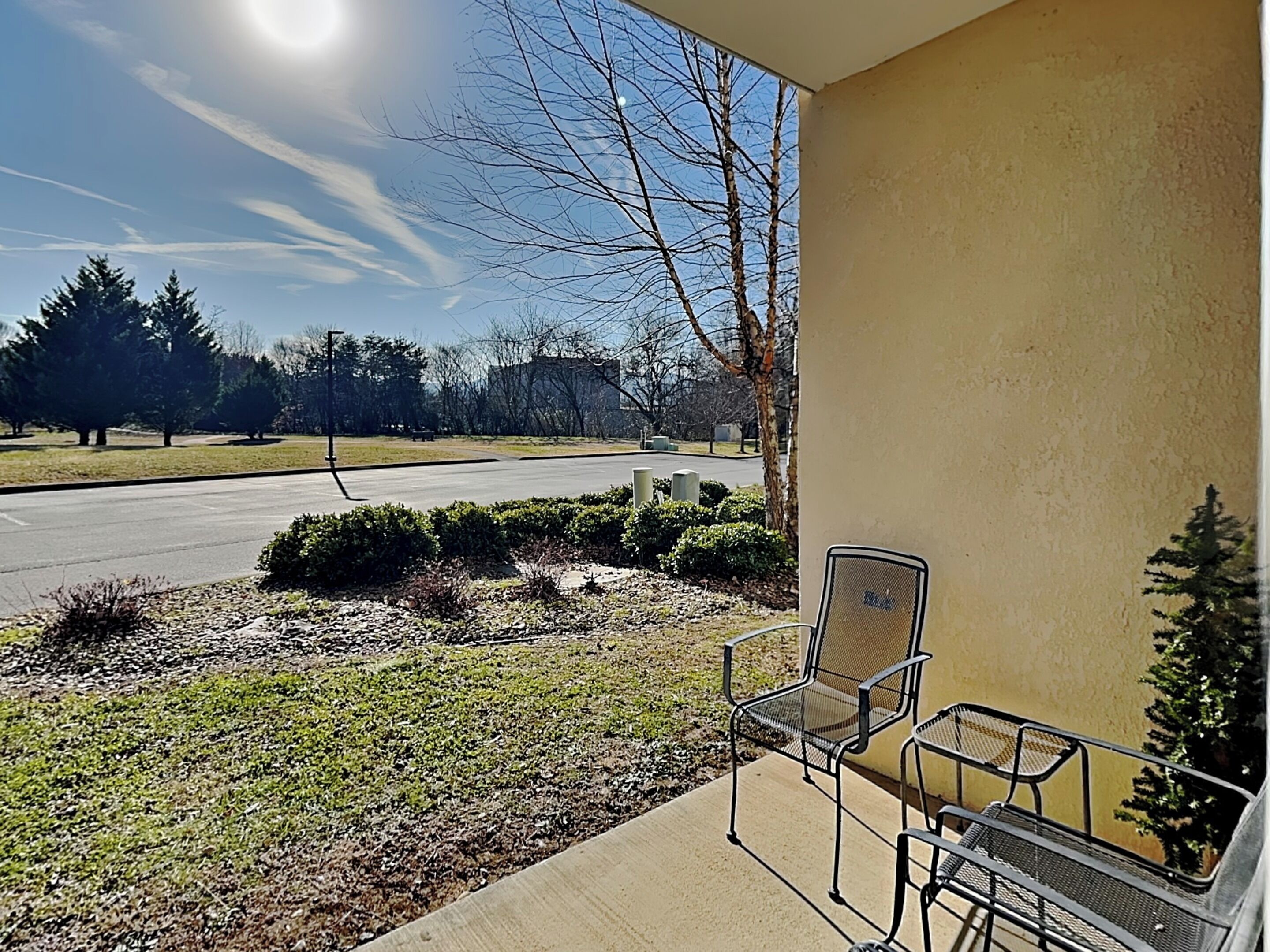 A covered outdoor area with a concrete floor, two metal chairs, and a small potted plant.