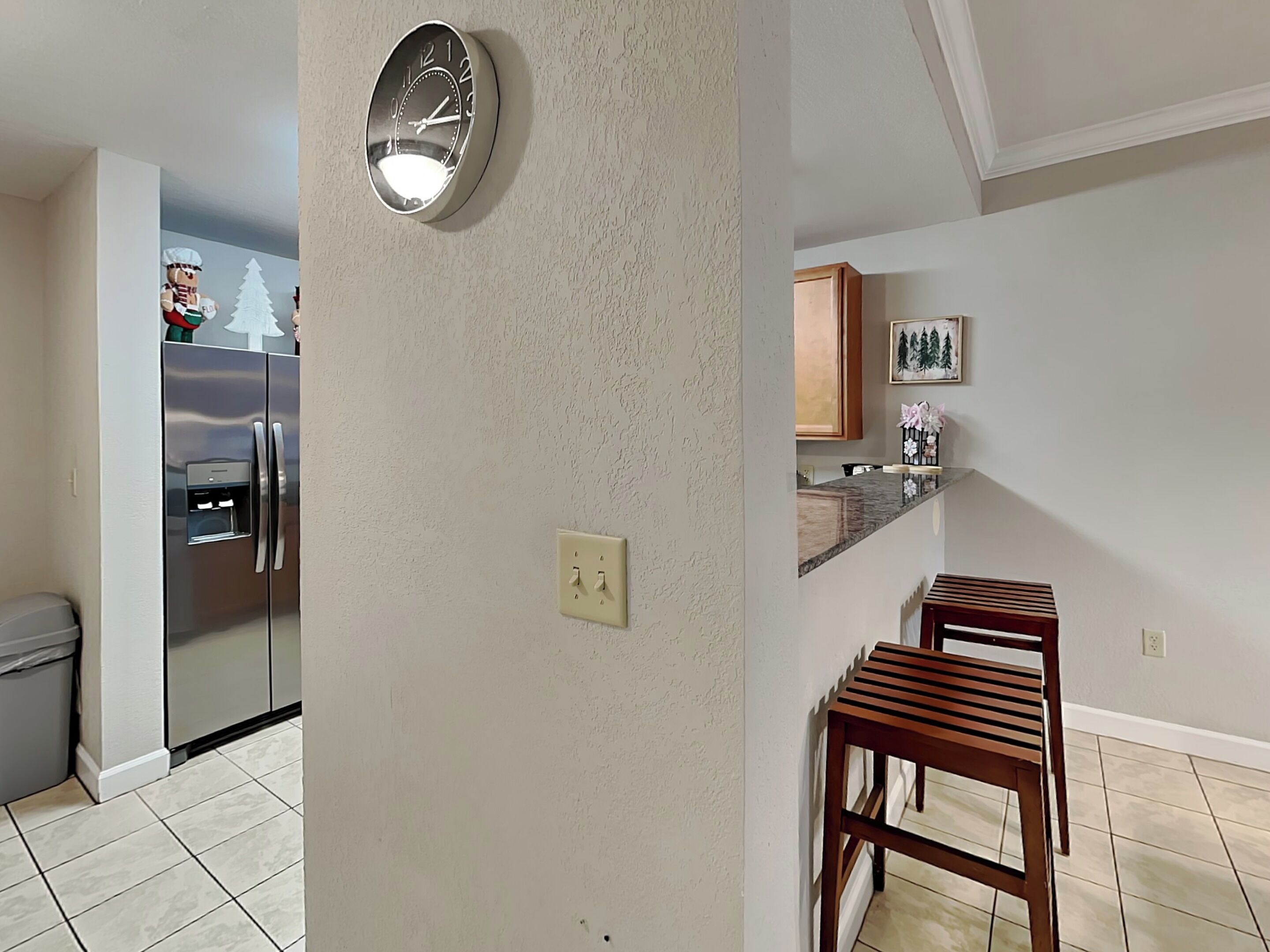 A kitchen with a stainless steel refrigerator, a wall clock, and a wooden bench.