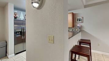 A kitchen with a stainless steel refrigerator, a wall clock, and a wooden bench.
