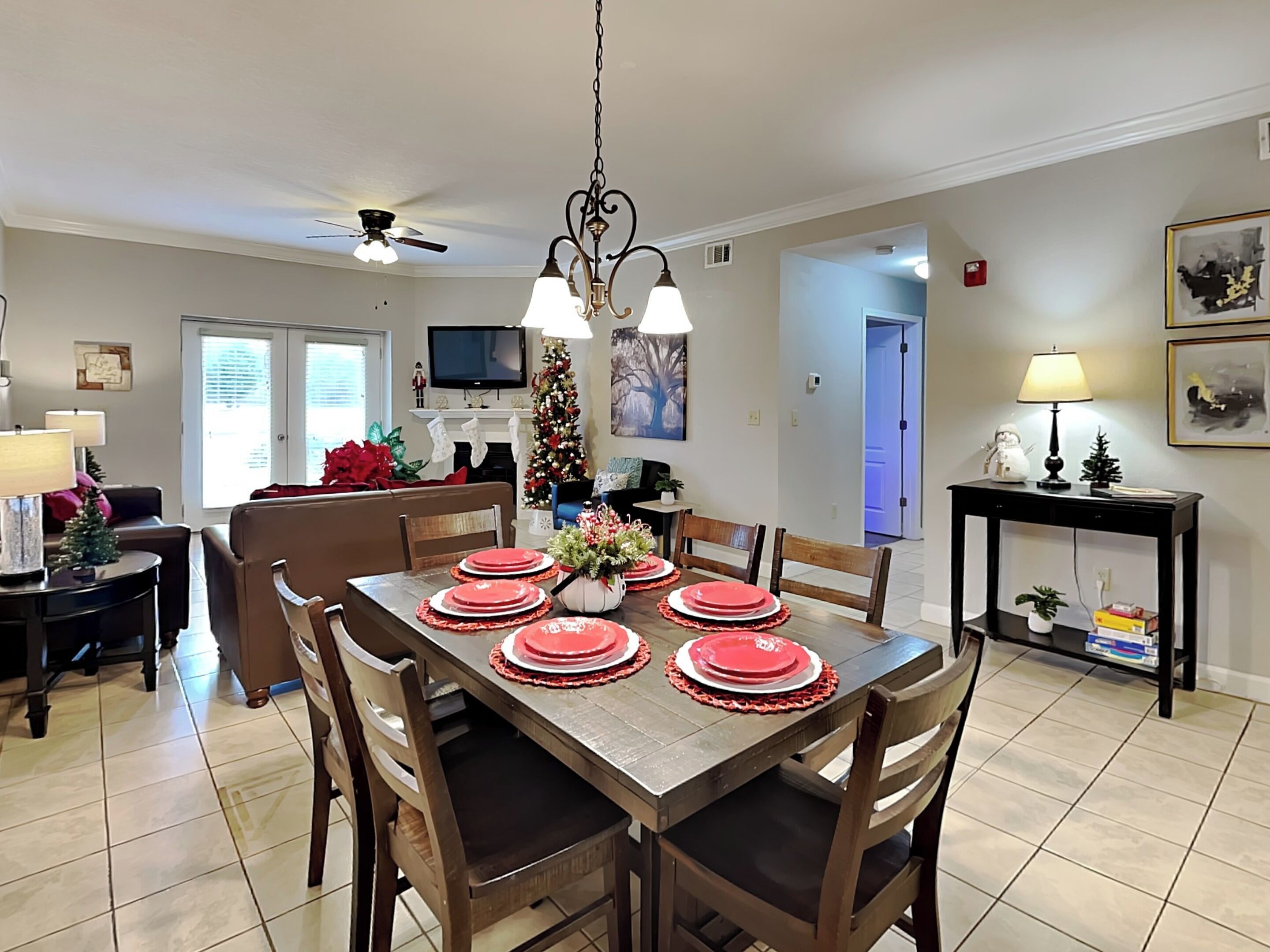 A dining area with a wooden table set for four, a ceiling fan, and a TV in the background.