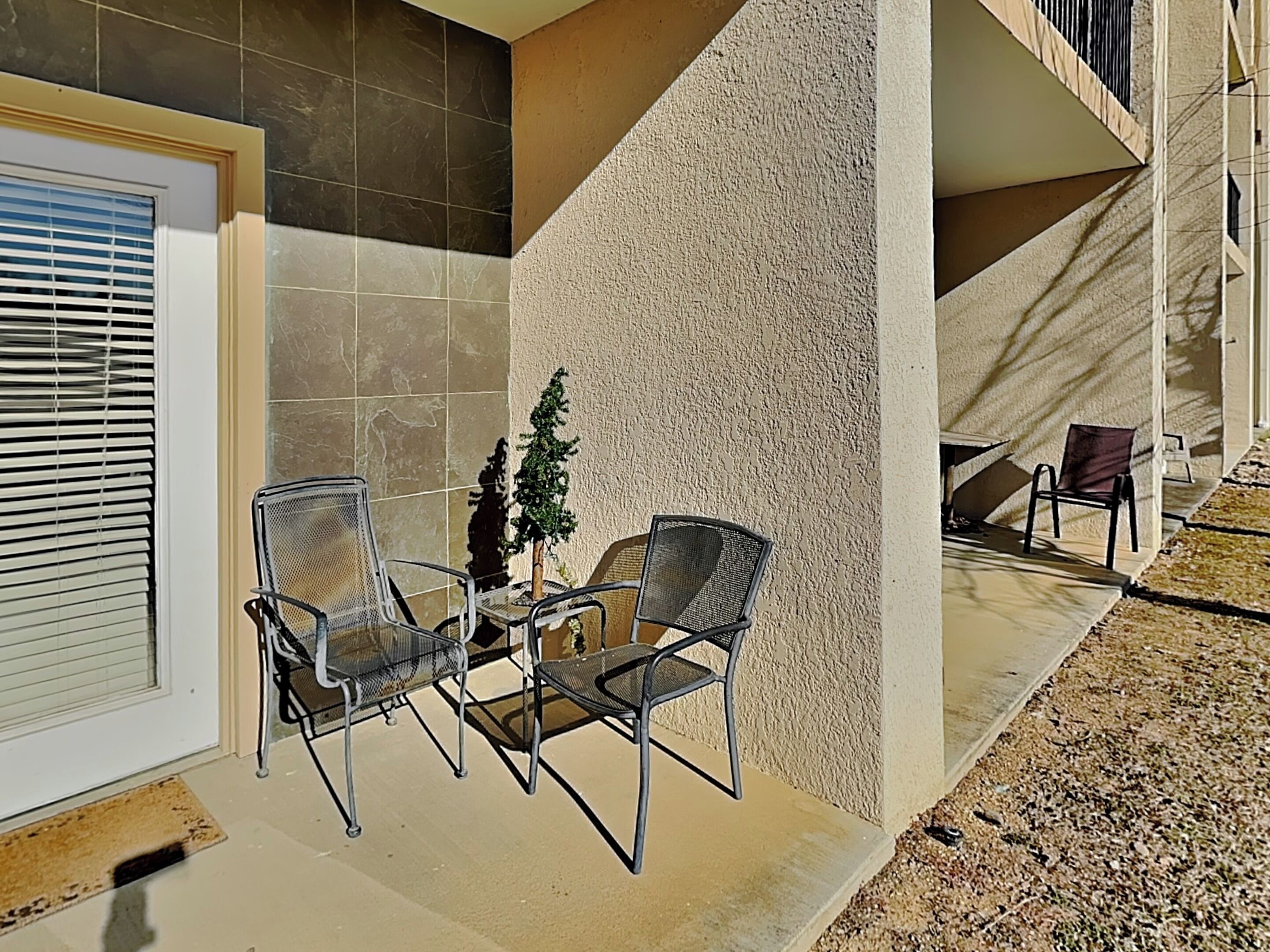 Eine Terrasse mit zwei Metallstühlen, einem kleinen Topfpflanzen und einer Tür mit Rollläden.