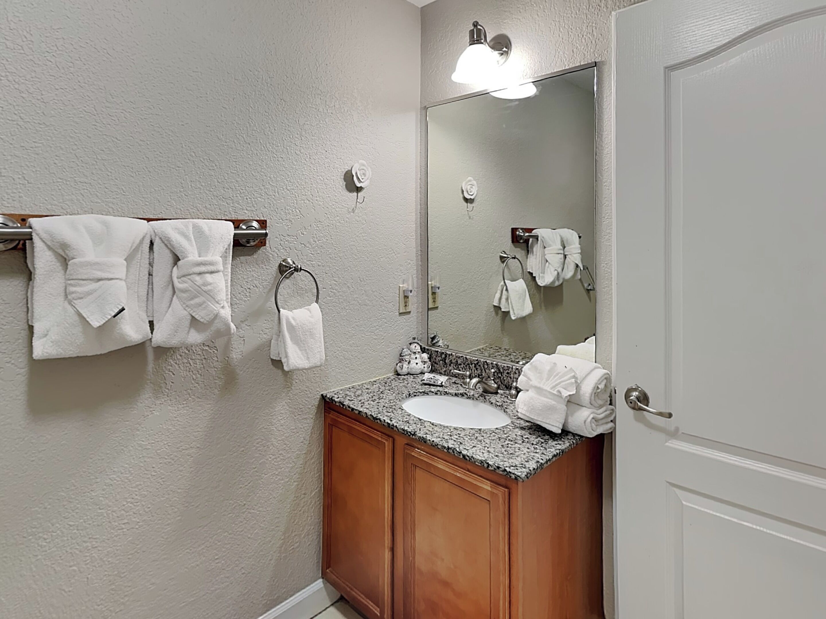 A bathroom with a granite countertop sink, wooden cabinets, a mirror, and multiple white towels hanging on towel racks.