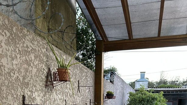 Ein überdachter Patio-Bereich mit einer Steinmauer, mehreren hängenden Pflanzgefäßen und zwei Korbstühlen.