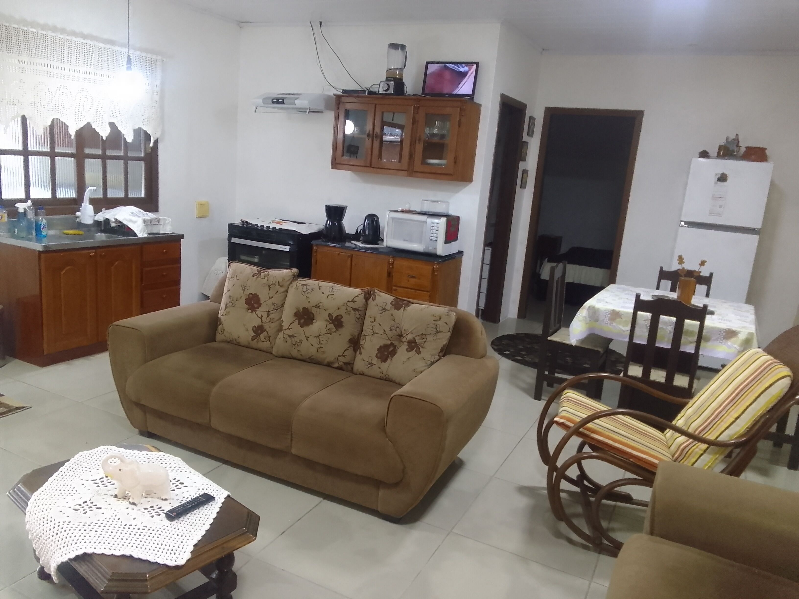 A living room with a sofa, a coffee table, a dining table with chairs, a kitchen area with cabinets, and a refrigerator.
