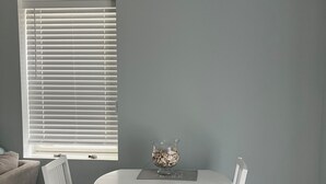 A dining area with a round table, two chairs, a glass vase with decorative items, and a window with blinds.