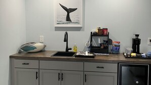 A kitchen with a sink, countertop, cabinets, a coffee maker, and a whale tail artwork on the wall.