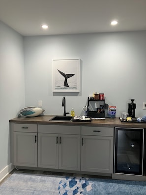 A kitchen with a sink, countertop, cabinets, a coffee maker, and a whale tail artwork on the wall.