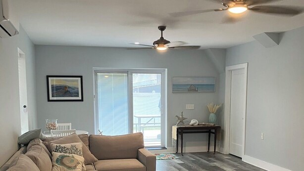 A living room with a sectional sofa, a ceiling fan, and a view to the outdoors.