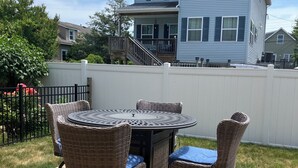 A deck with a round table and four wicker chairs, surrounded by a white fence.