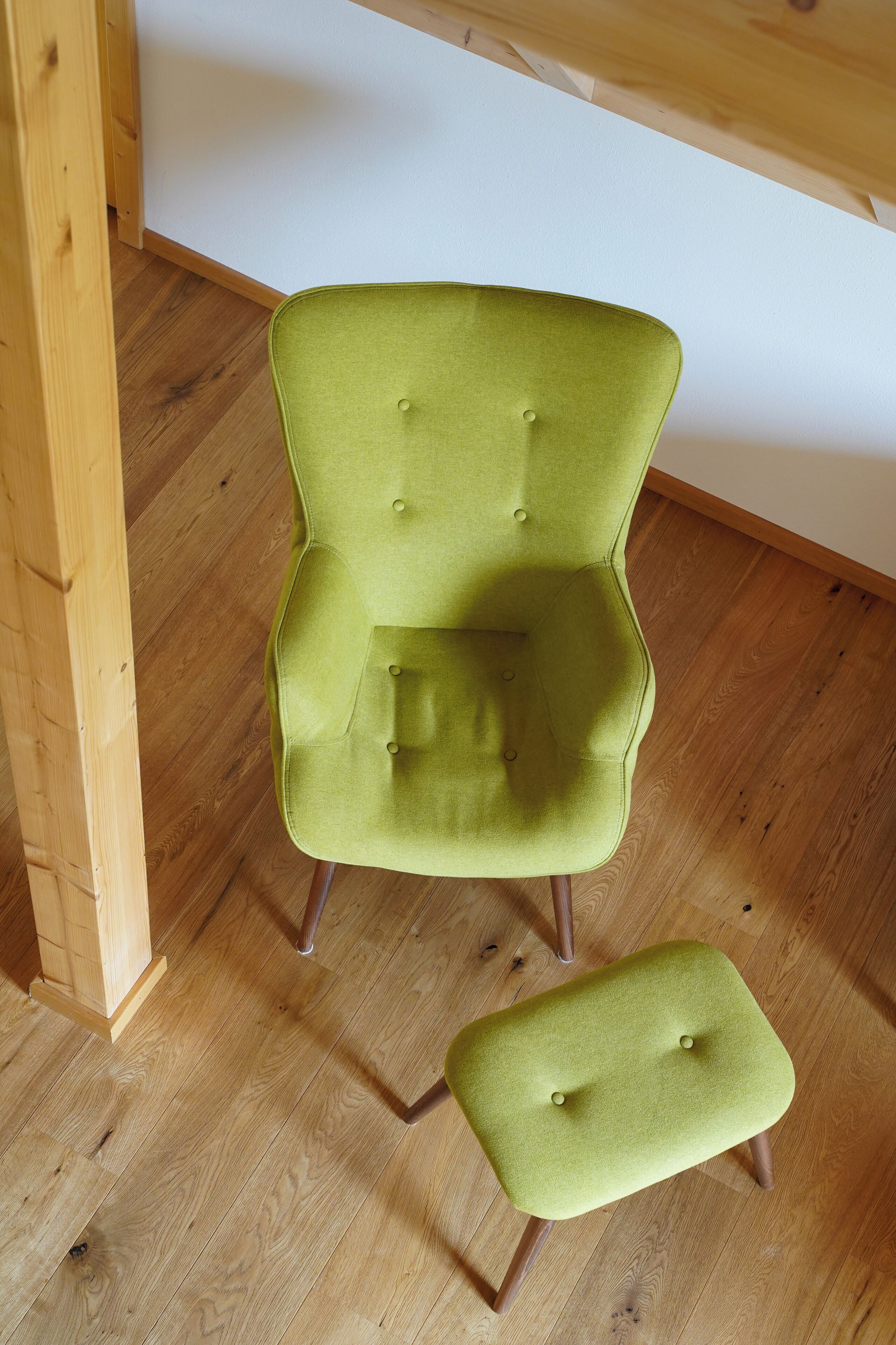 A green upholstered chair with a matching ottoman, wooden floor, and a wooden beam structure.