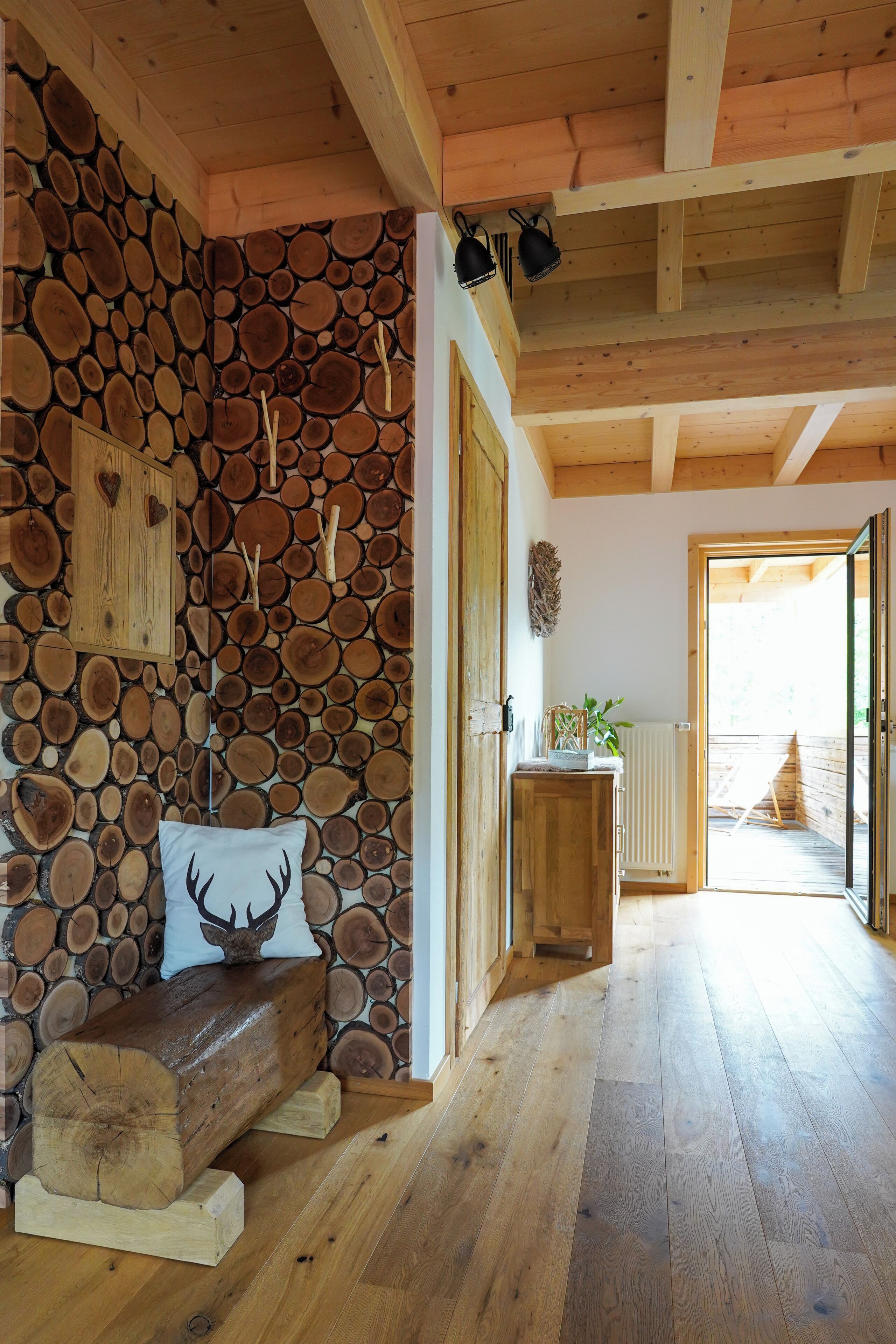 Ein Zimmer mit einer Holzwand aus Baumstämmen, einer Bank mit einem Deer-förmigen Kissen und einem Holztisch mit einer Pflanze.