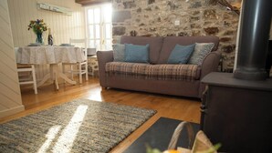 A cozy living room with a sofa, a table with chairs, a fireplace, and a rug. - Little Rogeston Cottage, Nolton Haven (Nolton Haven)